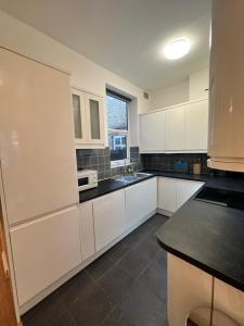 a kitchen with white cabinets and a black counter top at 2 Bedroom & Living Room Apartment In Paddington in London