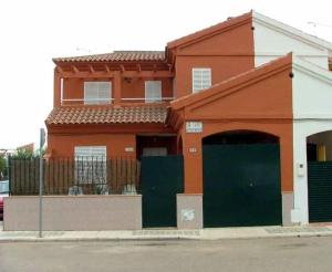un edificio naranja con puertas verdes y una valla en "Casa Colorá" en Sevilla, en Benacazón