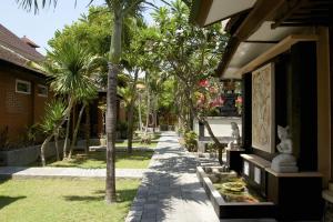 a walkway in front of a building with palm trees at Ayu Lili Garden Hotel Kuta in Kuta
