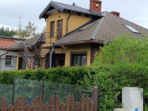 een geel huis met een zwart dak en een hek bij Apartament KNIEJA LUX in Tuchola