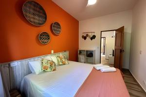 a bed in a room with an orange wall at Vila Saíra, chalé Laranja, 50m da praia in Ilhabela