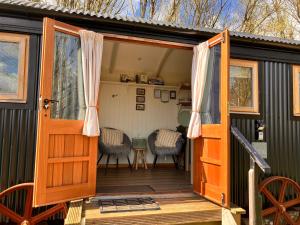 uma porta aberta de uma pequena casa com um deque em Archie the shepherd’s hut em Penruddock