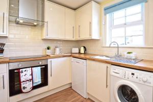 eine Küche mit weißen Schränken, einer Waschmaschine und einem Trockner in der Unterkunft Fordel Cottage in Dalkeith