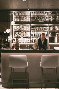a man standing behind a bar with two white stools at TRIFORÊT alpinresort in Hinterstoder