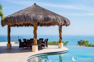 a table and chairs under a straw umbrella next to a swimming pool at Firepit Sunsets, Hot Tub Soaks, BBQ, Ocean Views in San José del Cabo
