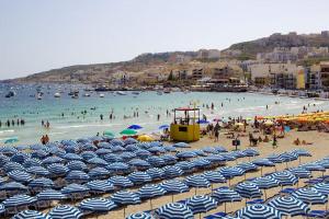 Une bande de parasols sur une plage avec des gens dans l'eau dans l'établissement Hillcrest 3 Bedroom Apartment, à Mellieħa