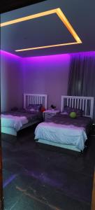 2 camas en una habitación con iluminación púrpura en منتجع سمايل, en Al-Qurayat