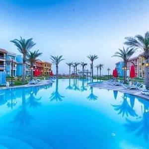 a large swimming pool with palm trees and buildings at Porto Matroh Tours in Marsa Matruh