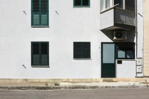 un bâtiment blanc avec des fenêtres vertes à volets et une porte dans l'établissement Viabalduini2, à Lecce