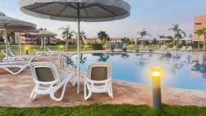 - un groupe de chaises et un parasol à côté de la piscine dans l'établissement mini-villa situee dans une residence Prestigia à Marrakech, avec une vue sur la piscine et le golf une securite 24h sur 24 et une proximite ideale de l aeroport 5 minutes C est une offre parfaite pour des vacances, à Marrakech