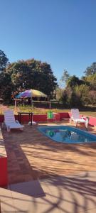 a swimming pool with two chairs and an umbrella at Pousadinha RoSi. in Santa Bárbara do Rio Pardo