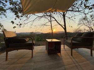 een patio met 2 stoelen en een tafel met uitzicht op de zonsondergang bij Cozy Cottage on hilltop near Conchal - Casa Huella in Matapalo
