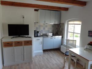 a kitchen with white cabinets and a flat screen tv at Ferienwohnung Düne in Krummhörn