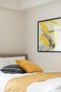 a bed with a yellow pillow and a painting on the wall at SG RESIDENCE INN HAKATA in Fukuoka