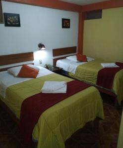 Habitación de hotel con 2 camas con sábanas amarillas y rojas en Hospedaje Del Carmen, en Machu Picchu