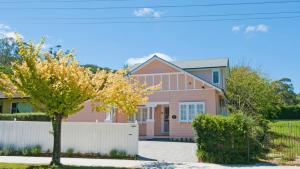 a pink house with a white fence and a tree at Plum Tree Cottage in Bowral