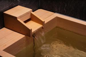 une chute d'eau avec un banc en bois dans une piscine d'eau dans l'établissement SHIROIYA HOTEL, à Maebashi