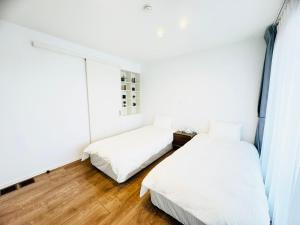 two beds in a room with white walls and wooden floors at Akikawa Koshi 2 プレミアム鉄骨 一棟貸切ヴィラ in Yuge