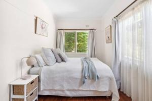 a white bedroom with a bed and a window at Capital Cottage in Narrabundah