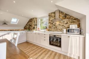- une cuisine avec des placards blancs et un mur en pierre dans l'établissement Blar Cottage (Private Sauna + Fast Starlink Wifi), à Hayfield