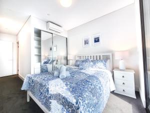 Schlafzimmer mit einem Bett mit einer blauen und weißen Bettdecke in der Unterkunft Hamptons Style 2BR & kid room w view in Olympic Park in Sydney