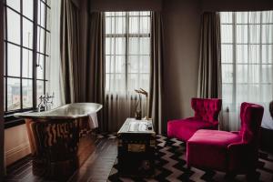 a room with a tub and a chair and windows at Hotel Gotham in Manchester
