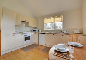uma cozinha com armários brancos e uma mesa em Oak Tree Cottage em Old Buckenham
