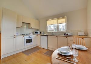 a kitchen with white cabinets and a table in it at Oak Tree Cottage in Old Buckenham