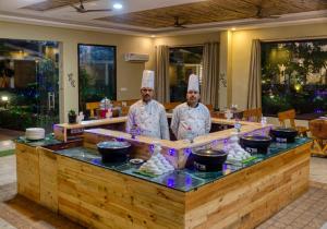 two chefs standing behind a counter in a restaurant at De Floresta Resort in Rāmnagar