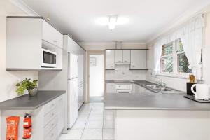 una cocina blanca con armarios blancos y fregadero en Single Room in Pymble Sleeps 1, en Pymble