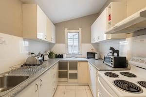 a kitchen with white cabinets and a sink and a stove at Private Ensuite Queen room near Sydney Airport in Sydney