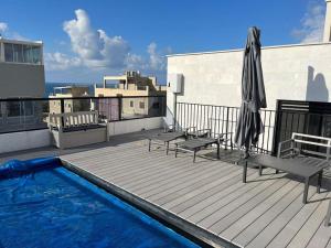 una terrazza all'ultimo piano con ombrellone, panchine e piscina di נוף נתניה a Netanya