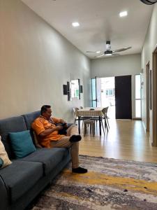 a man sitting on a couch in a living room at D' Permata Homestay Kulim in Kulim
