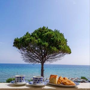 a table with two cups and plates of food and a tree at Red Sun Apartments in Amoudi
