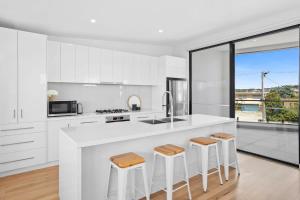 Una cocina con gabinetes blancos y una encimera con taburetes. en Seaside Style - Modern Coastal Retreat with Ocean Views, en Torquay