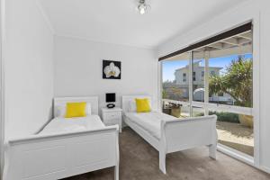 a white bedroom with two beds and a large window at Half Moon Bay Hideaway 1 min to Foreshore in Indented Head