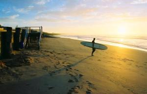 uma pessoa andando na praia com uma prancha de surf em Urban Executive Style Meets Relaxed Coastal Vibes em Ocean Grove