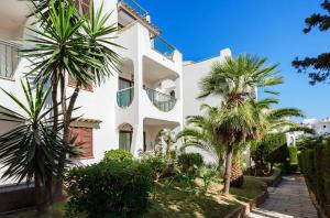 a white building with palm trees in front of it at Flipflop Surfing Playa in Santa Ponsa