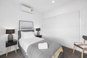 a white bedroom with a bed and a chair at Boardwalk on Bright Coastal Apartment in Torquay