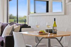 a table with two glasses of wine and a bowl of fruit at On The Esplanade - Ocean Front Apartment in Torquay
