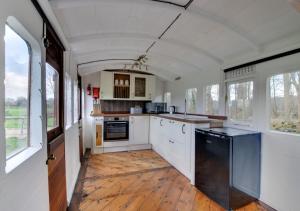 a kitchen with white cabinets and wooden floors and windows at The Railway Carriage in Briston