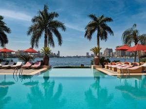 a swimming pool with chairs and palm trees and water at Sofitel Cairo Nile El Gezirah in Cairo