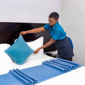 una mujer poniendo almohadas azules en una cama en Velmont Hotel, en Dar es Salaam