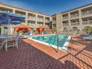 a swimming pool with tables and umbrellas next to a building at La Quinta by Wyndham San Francisco Airport West in Millbrae