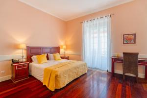 a bedroom with a bed and a desk and a window at O Cantinho da Mariazinha in Funchal