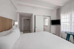 a white bedroom with a large bed and a television at Townhouse Hotel by LuxUrban in Miami Beach