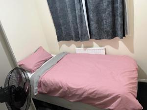 Cama pequeña con sábanas rosas y ventana en 3 bedroom mid terraced house (2 double & 1 single) en Grays Thurrock