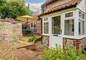 a brick house with an umbrella and a patio at Dolphin Cottage in Wiveton