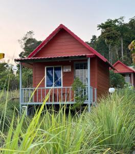 a small red house with a balcony in the grass at Maloop Cafe Bungalow in Koh Rong Island