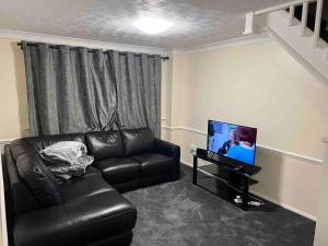 a living room with a leather couch and a television at 3 bedroom mid terraced house (2 double & 1 single) in Grays Thurrock